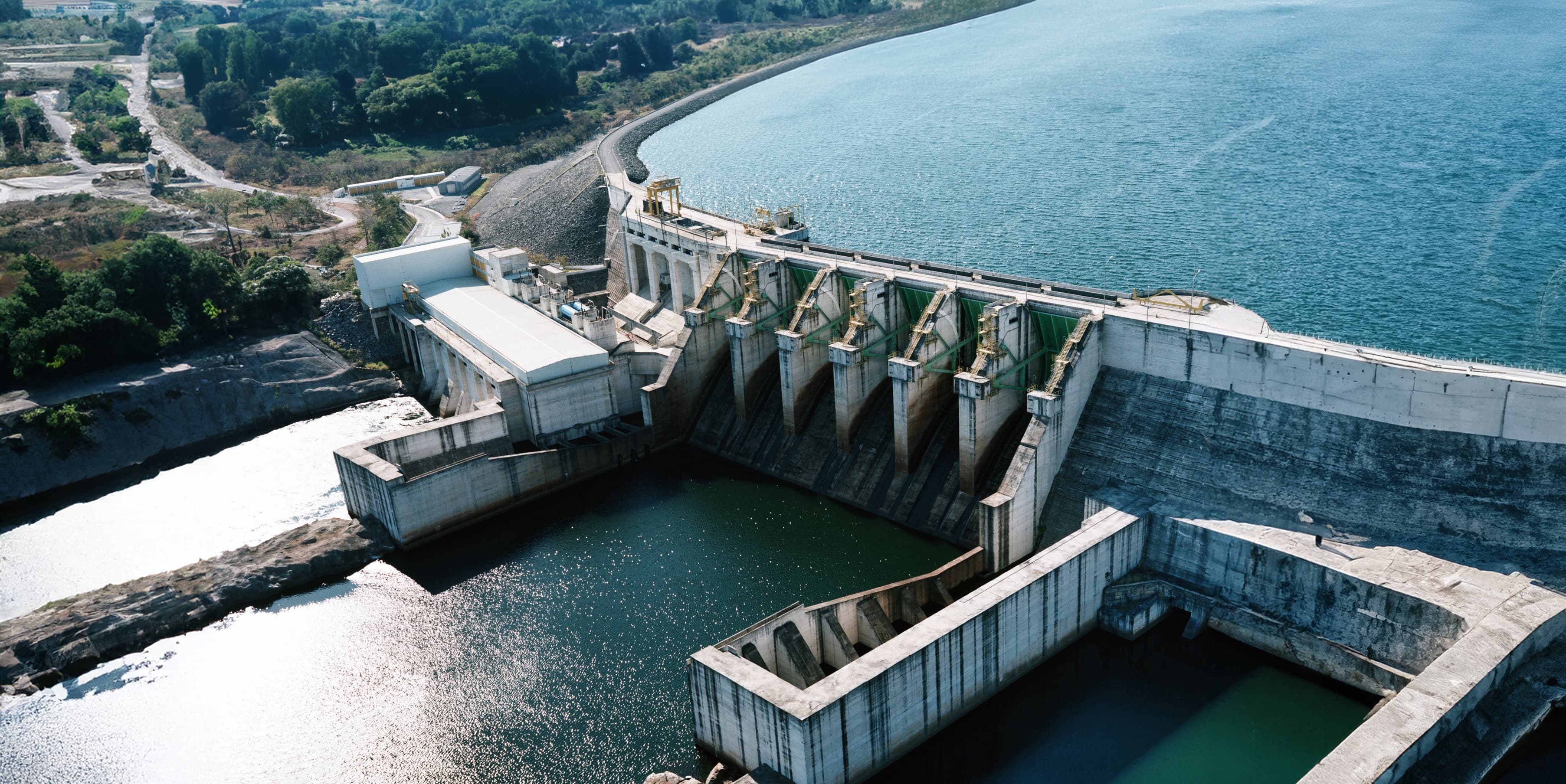 Großes Wasserkraftwerk mit mehreren Schleusen und einem weitläufigen Stausee, umgeben von natürlicher Landschaft.