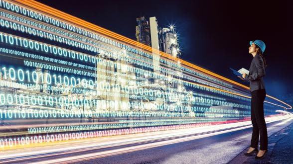 Engineer in front of a virtual wall of data and numbers, with a futuristic factory in the background.