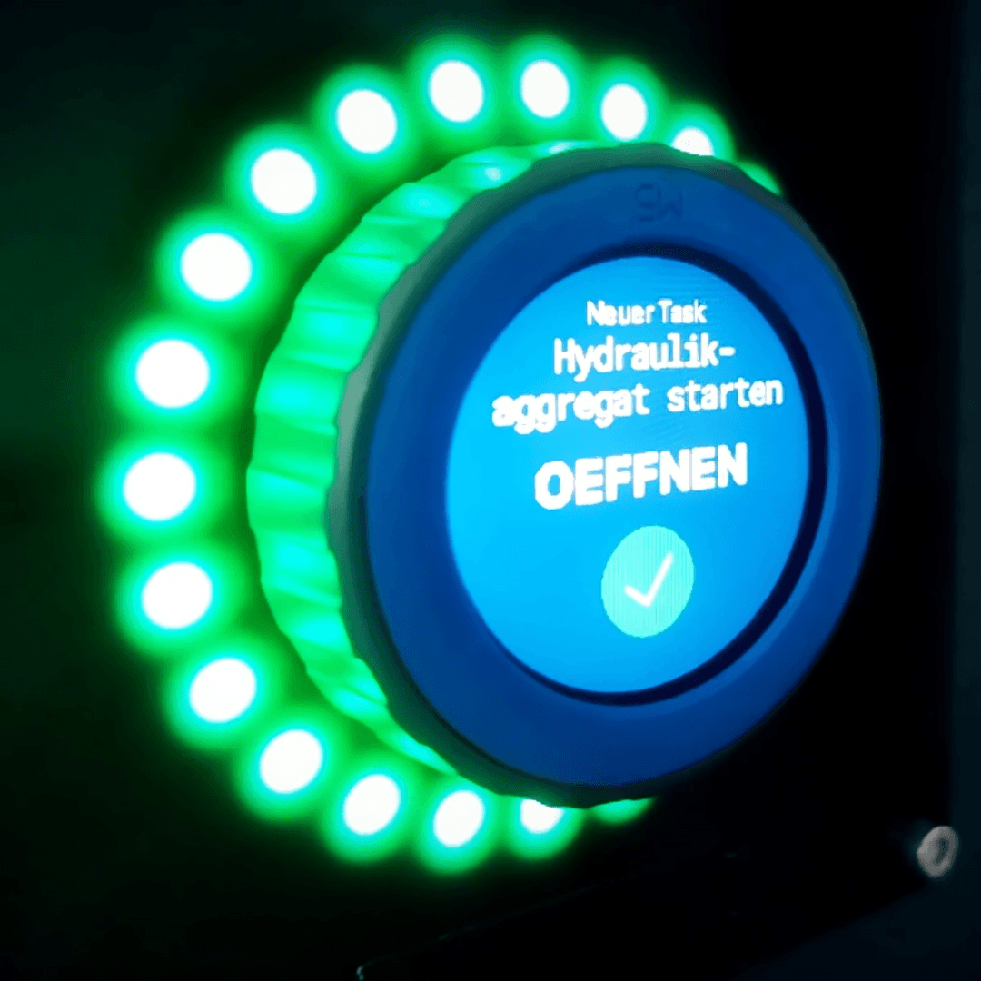 Illuminated smart control button with a digital display showing a task command in German.