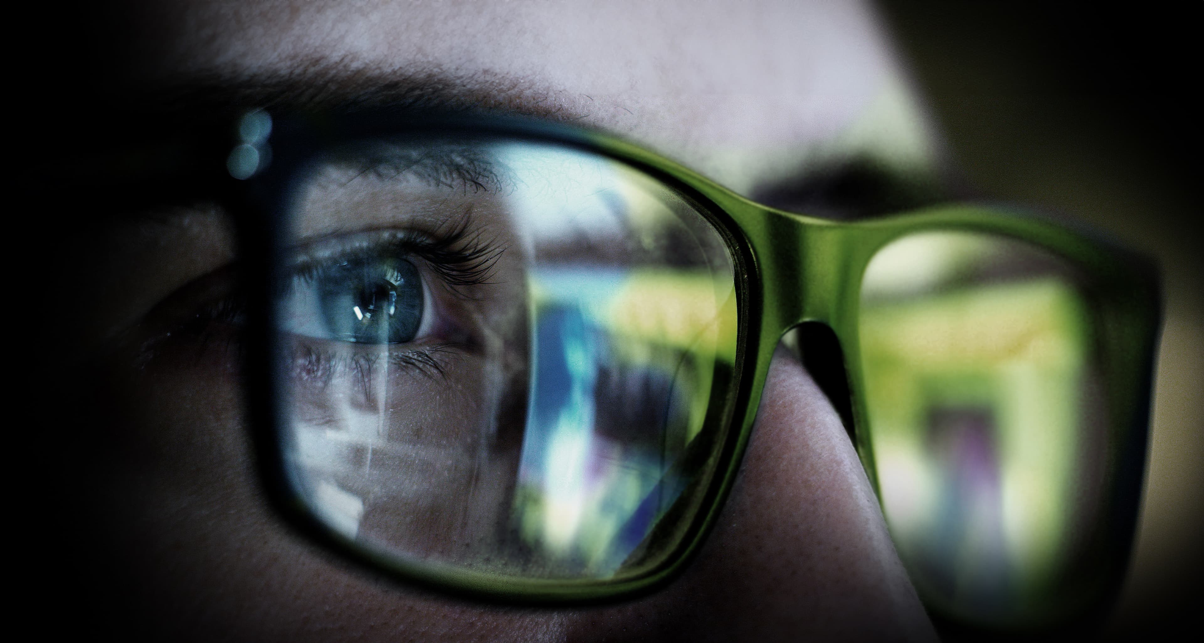 Close-up of a person's eye behind glasses, with digital content reflected in the lenses.
