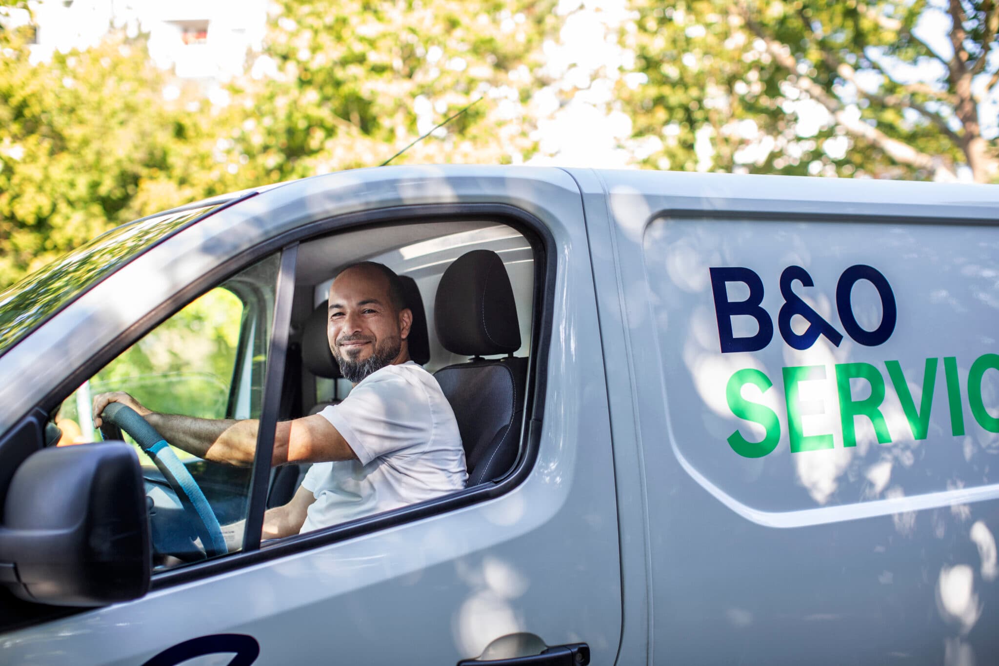 B&O Service Mitarbeiter mit verschränkten Armen in blauem Pullover in einem Flur mit Rohren an der Decke. Wartung oder Service im Hintergrund.