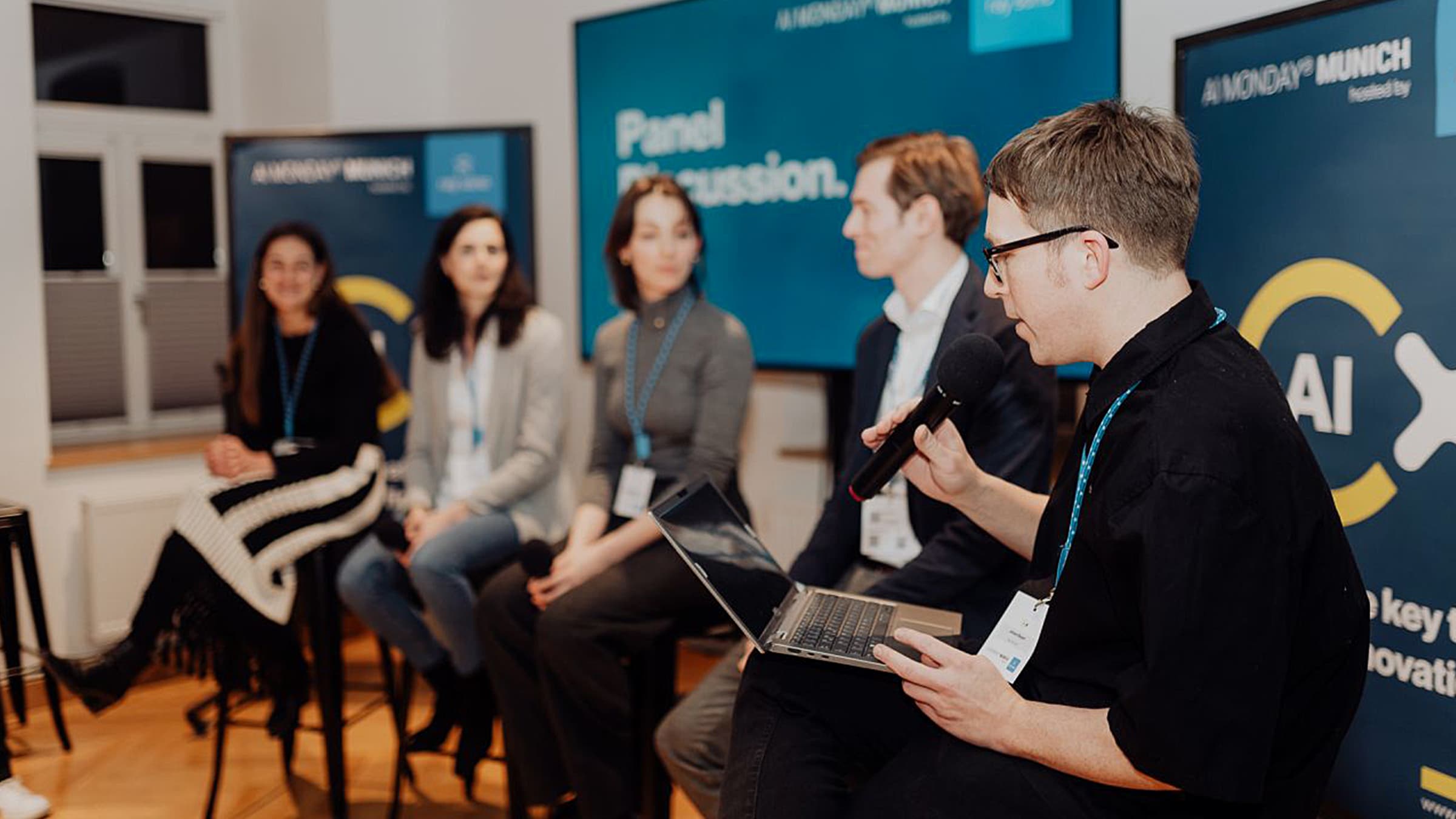 Panel discussion at "AI Monday" in Munich. Johann Bayerl and speakers, audience in background. Focus on AI innovations.