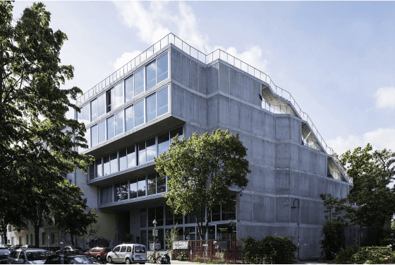 Ray Sono Office located in Lobe Block in Berlin with large glass windows on a street corner, surrounded by trees and parked cars.