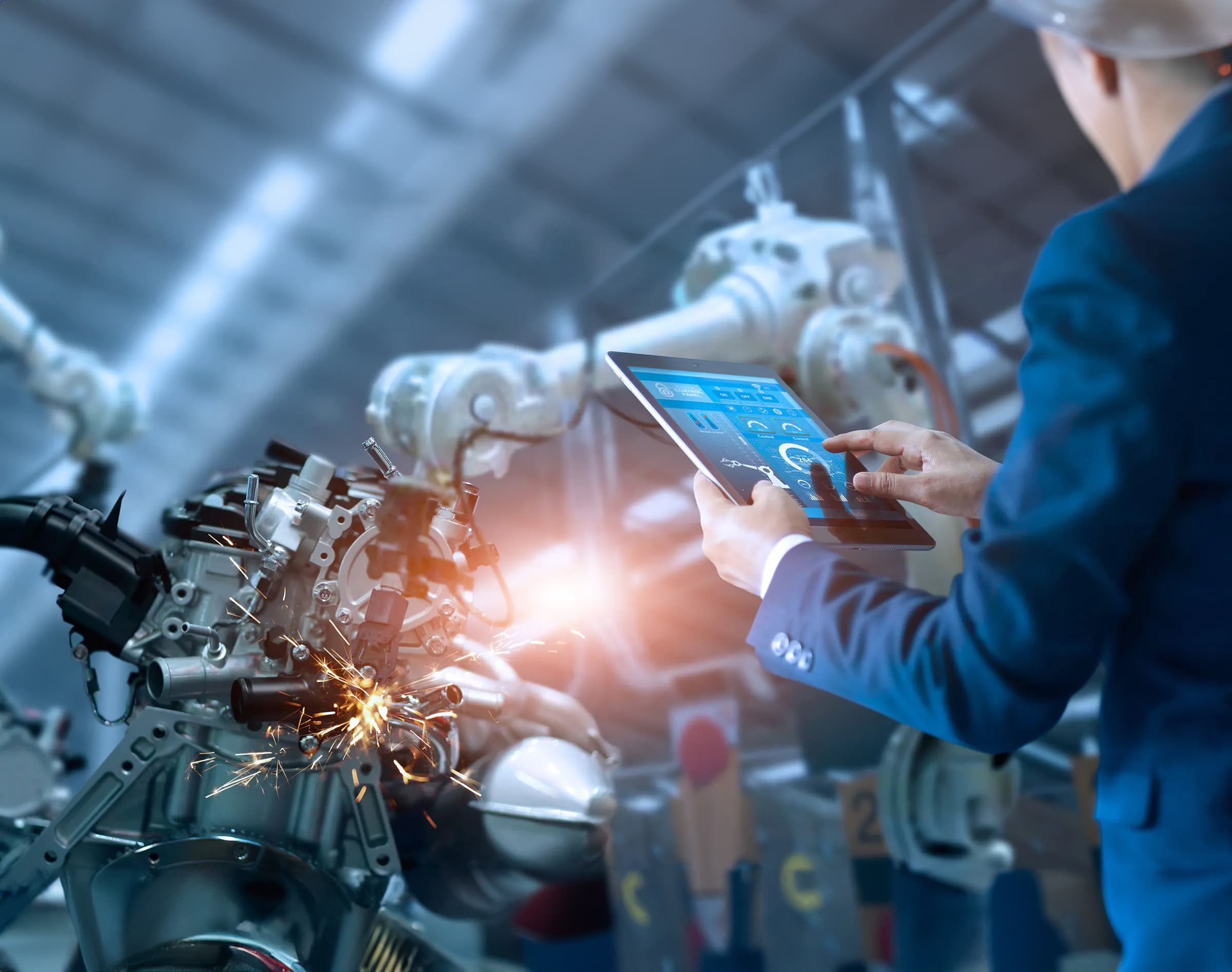 Engineer controlling robotic arms in an automated manufacturing facility using a digital tablet.